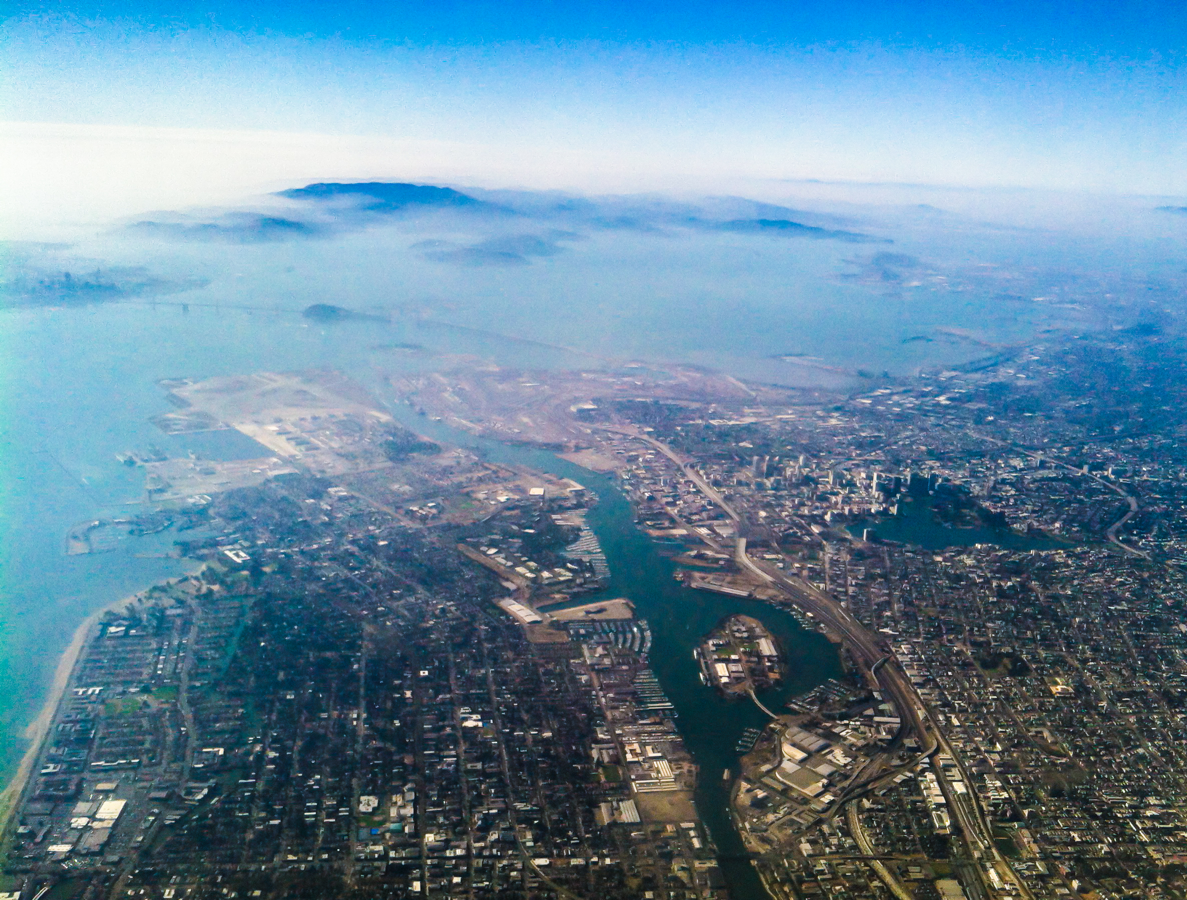 View of a metropolis on a bay with water interpenetrating the city and distant mountains emerging from the morning fog.